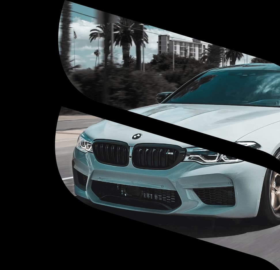 Viene mostrata una BMW bianca su una strada con palme e edifici sullo sfondo.